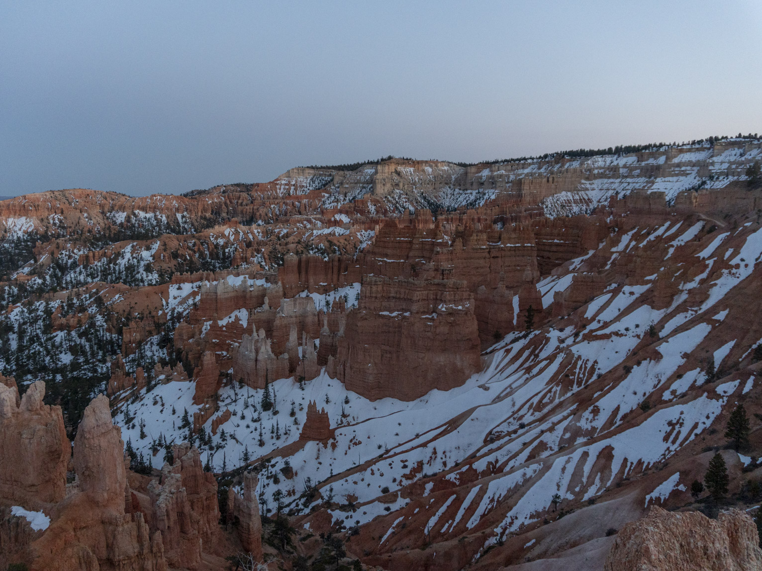 A view of an orange canyon and hoodoos partially covered with snow